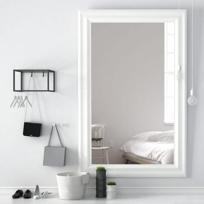Scandinavian entrance lobby hall with mirror reflecting bright bedroom with bed, chair and table lamp, minimalist white interior design