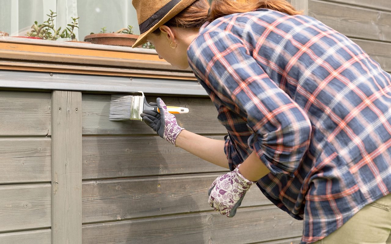 Woman worker painting wooden house exterior wall with paintbrush and wood protective color