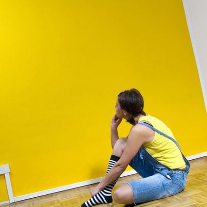 Woman sitting on floor, looking at yellow wall