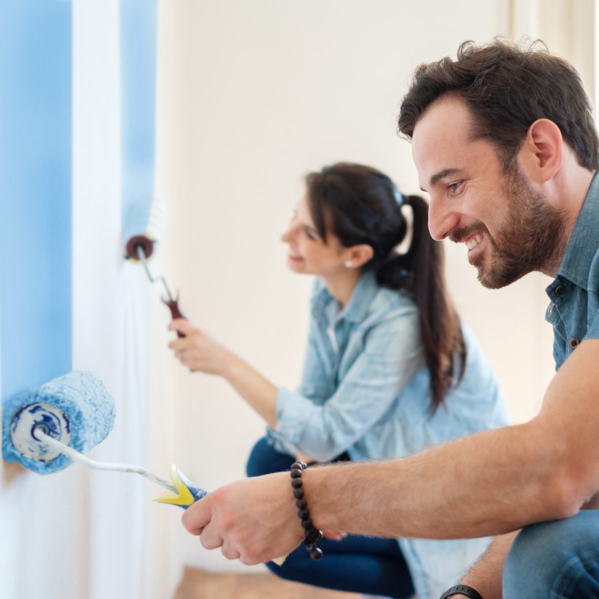 Young couple painting walls in their new house, do it yourself concept