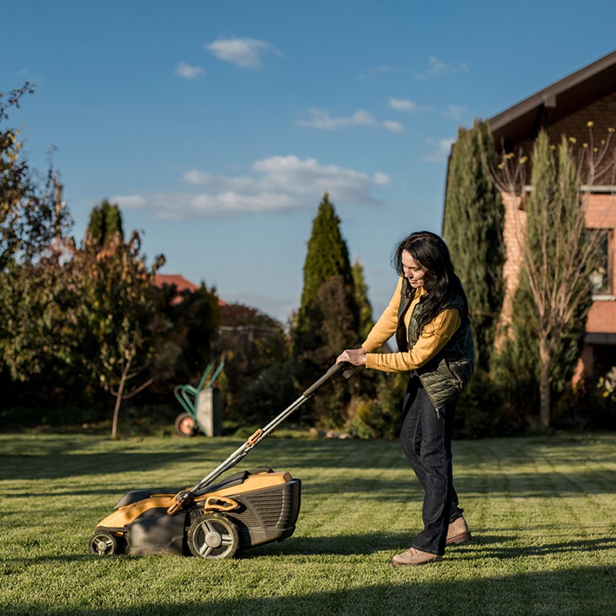 Woman Mowing Grass With Lawn Mower On Sunny Day