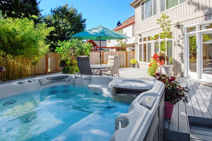 view of a hot tub in the foreground with a deck, outdoor table and chairs, and a house in the background