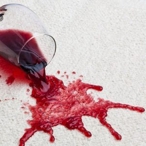 A toppled glass of red wine with a dirty carpet.