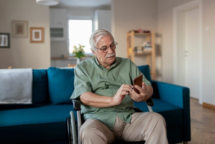 Handicapped Senior Man Sitting in a Wheelchair and Using a Smartphone