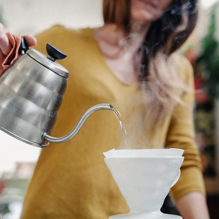 A woman pouring coffee from a pot through a paper filter.