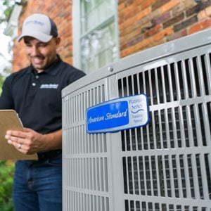 Close up on logo of Platinum 20 Heat Pump / Air Conditioner placed outside while American Standard technician makes notes