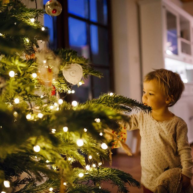 A small toddler girl looking at Christmas tree lights indoors