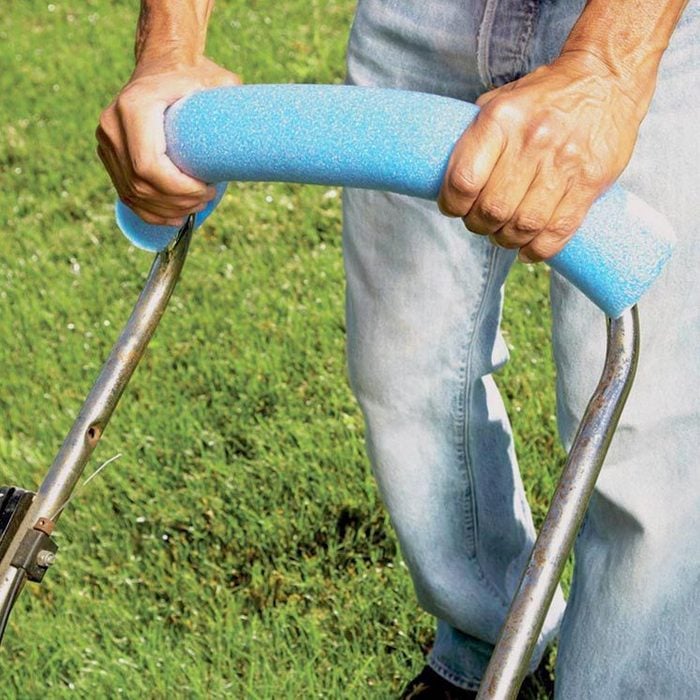 a man holding a lawn mower handle that has a blue pool noodle on it for comfort