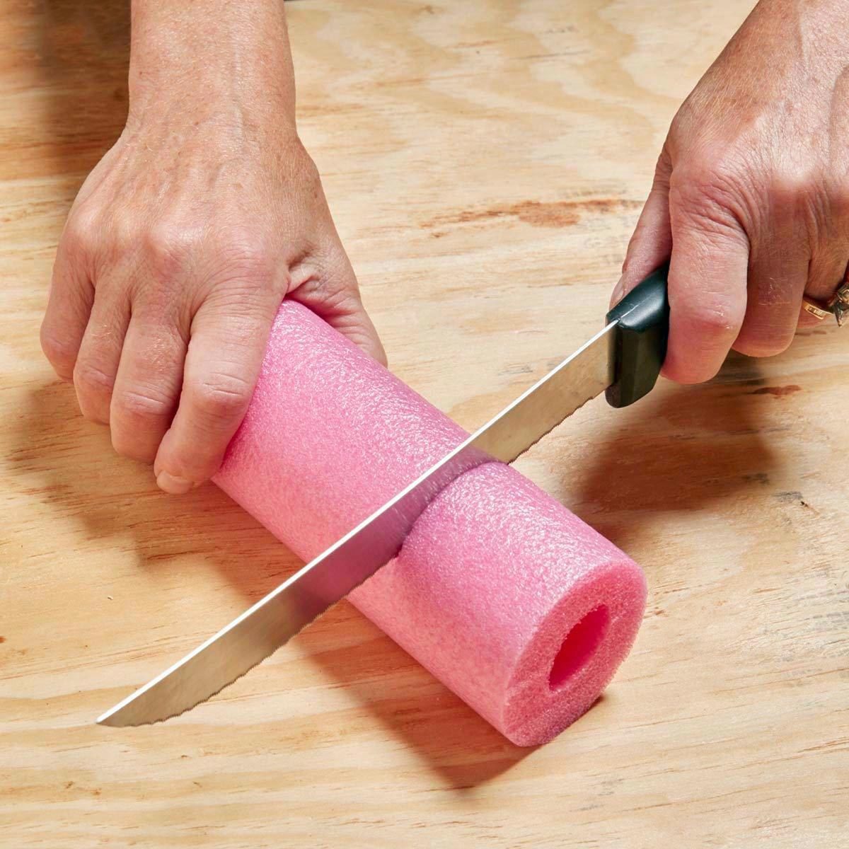 using a knife to cut a section off of a pink pool noodle