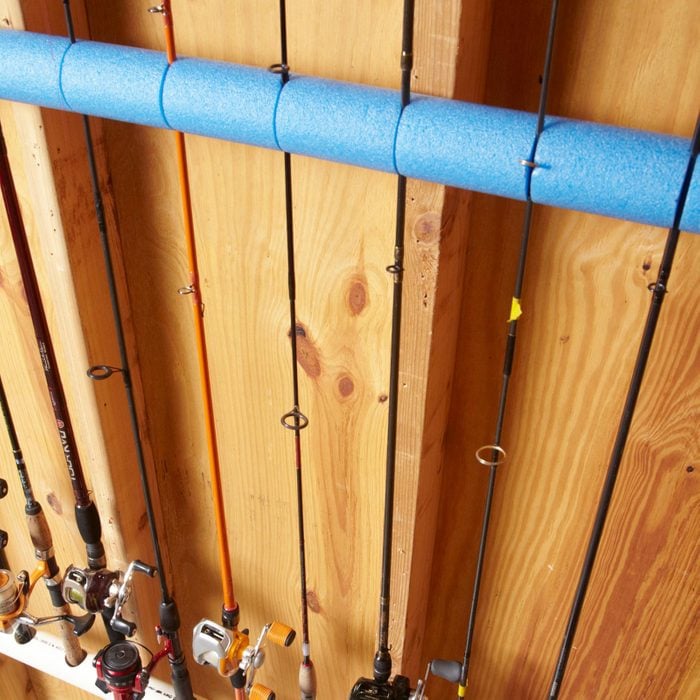 fishing poles placed in a blue a pool noodle with slits cut in it, hanging on a wooden garage wall
