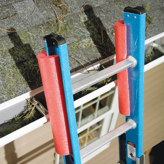 the top of a ladder near the gutters of a house with pool noodles at the top of the ladder to protect the part of the house it is leaning against
