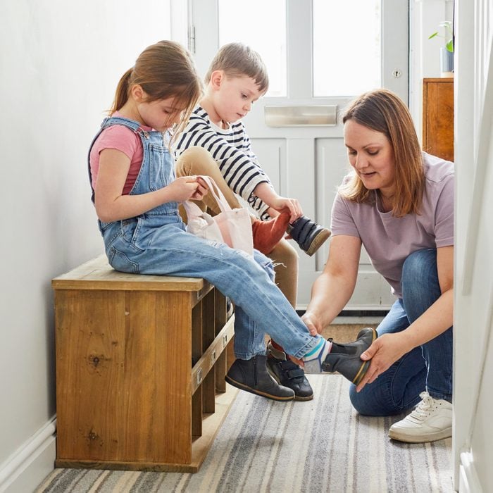 Young children getting shoes on ready to leave the house with mother helping