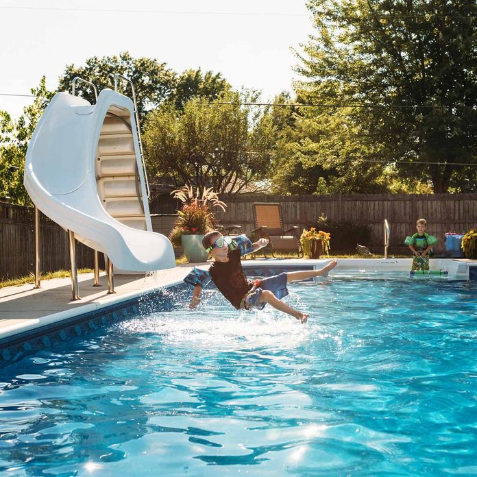 Boy looking at brother jumping in swimming pool on sunny day water slide Gettyimages 961076954 Slide