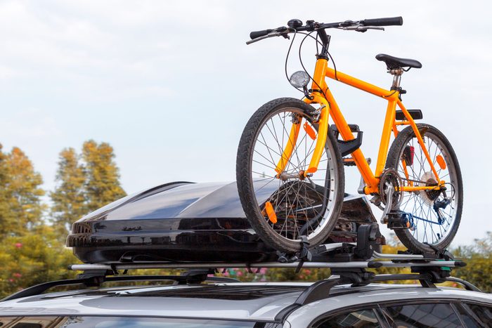 cargo box and orange bicycle attached to a roof rack on a car