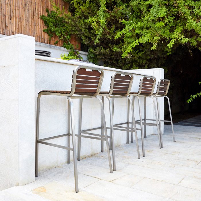 Four empty bar stool chairs with wooden seats and metal foot near a white concrete bar counter