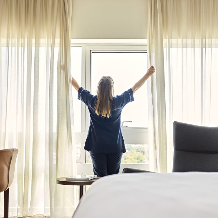 Chambermaid opening curtains of window in hotel room