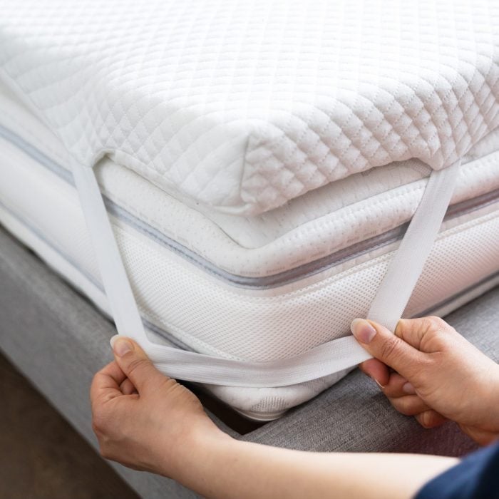 womans hands securing a mattress topper to a mattress