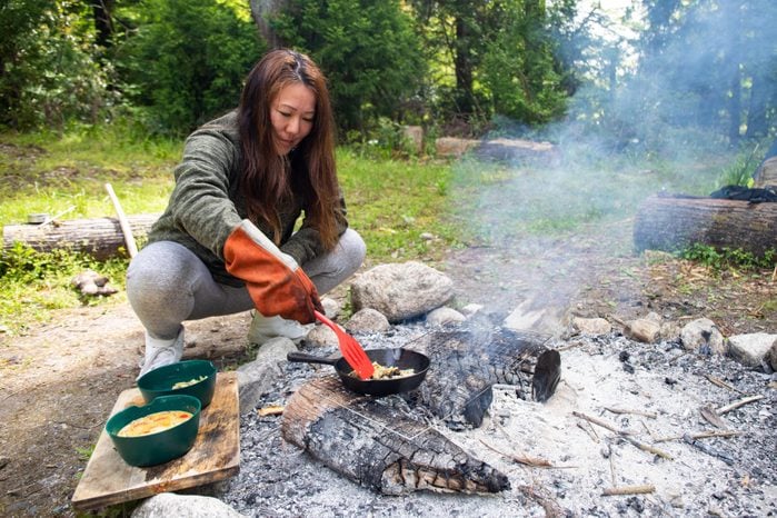 woman using a spatula while cooking over a campfire