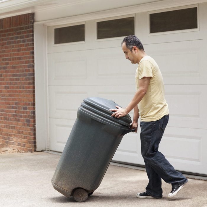 Hispanic man rolling garbage can