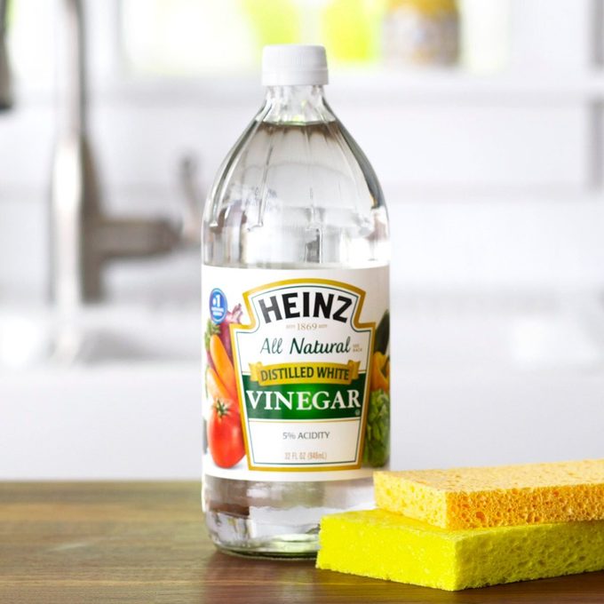 Vinegar and cleaning sponges on wooden surface