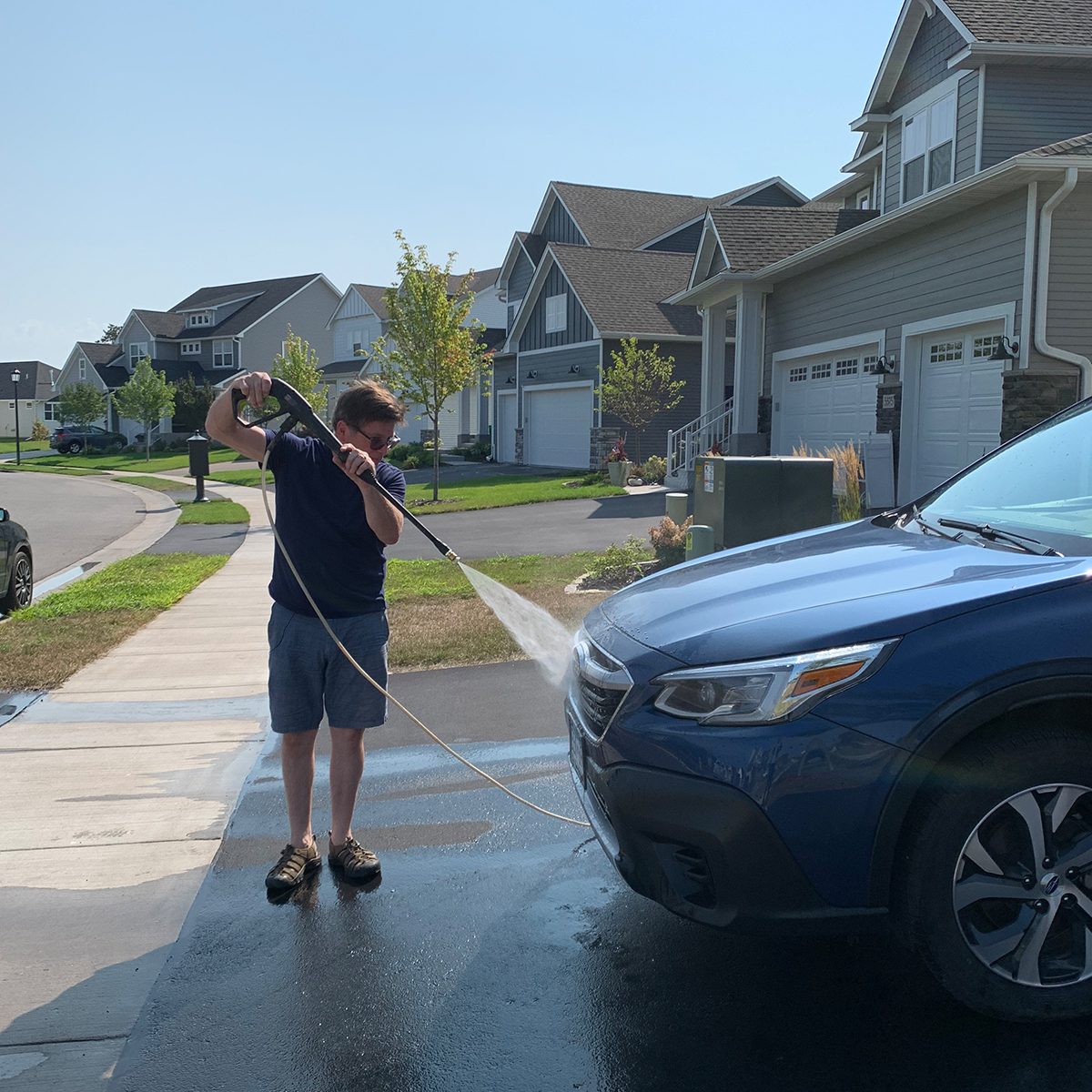 man pressure washing his car in driveway