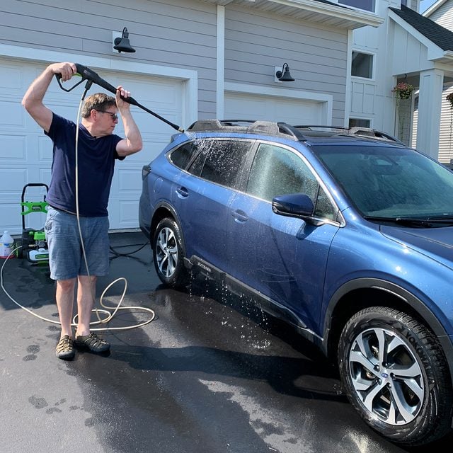 man pressure washing his car in driveway
