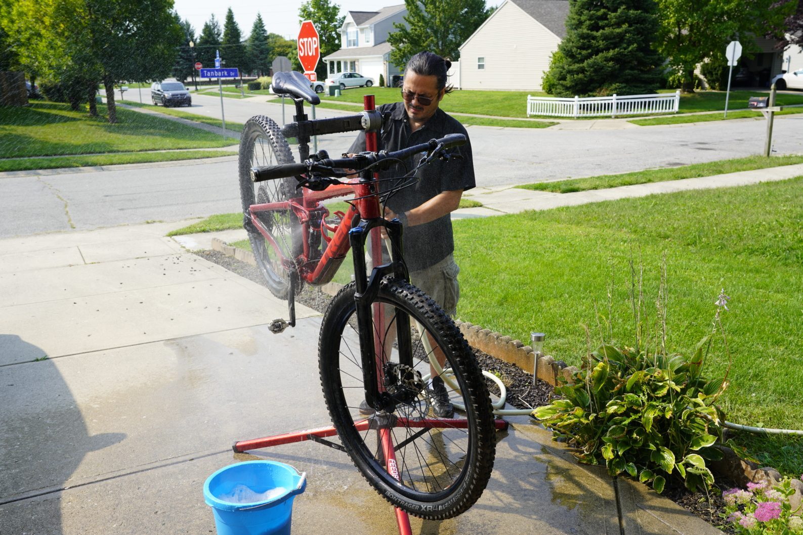 man cleaning his bike with a hose in the driveway