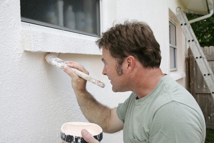 man painting the stucco exterior of a home