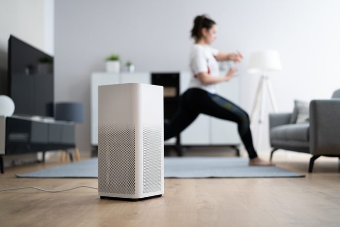 Young Woman Using Air Ionizer at home while she does yoga in the background