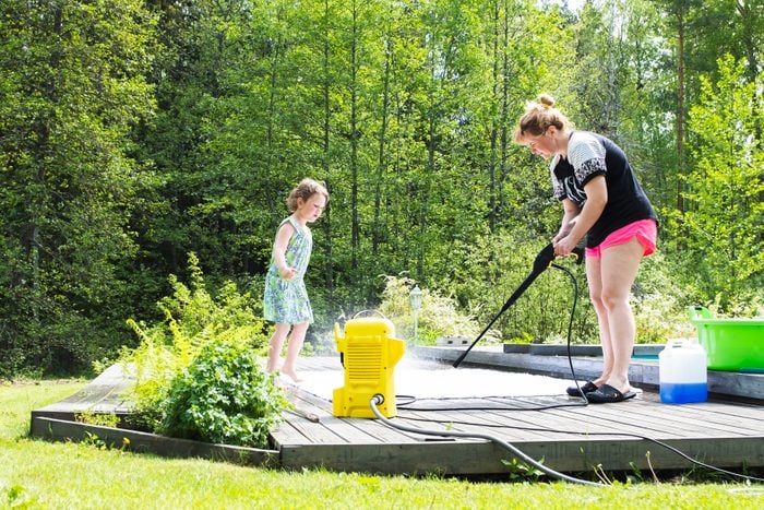 a woman with her child pressure washing an outdoor rug outside on the deck