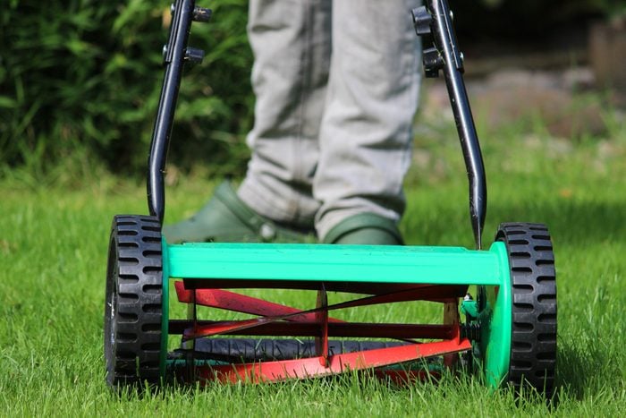 close up of person using a manual push lawn mower in back yard
