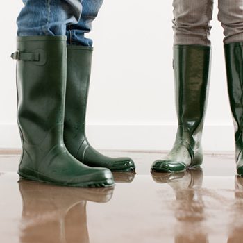 Young couple in rubber boots on flooded floor in home