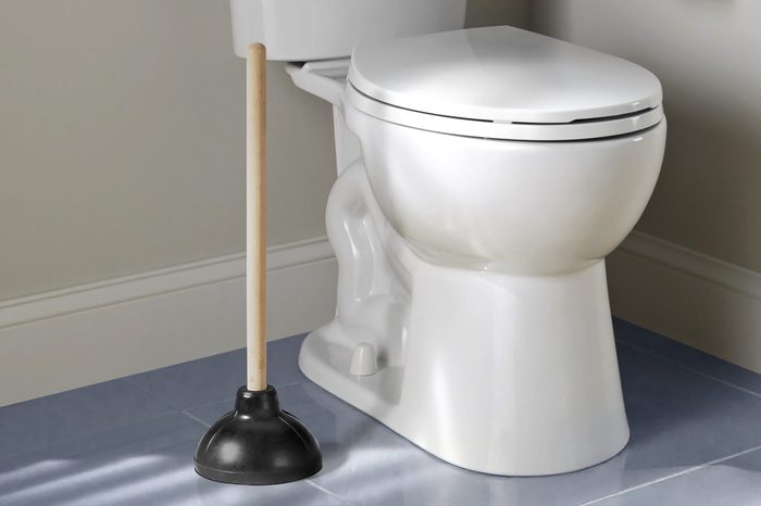Toilet plunger beside toilet in bathroom