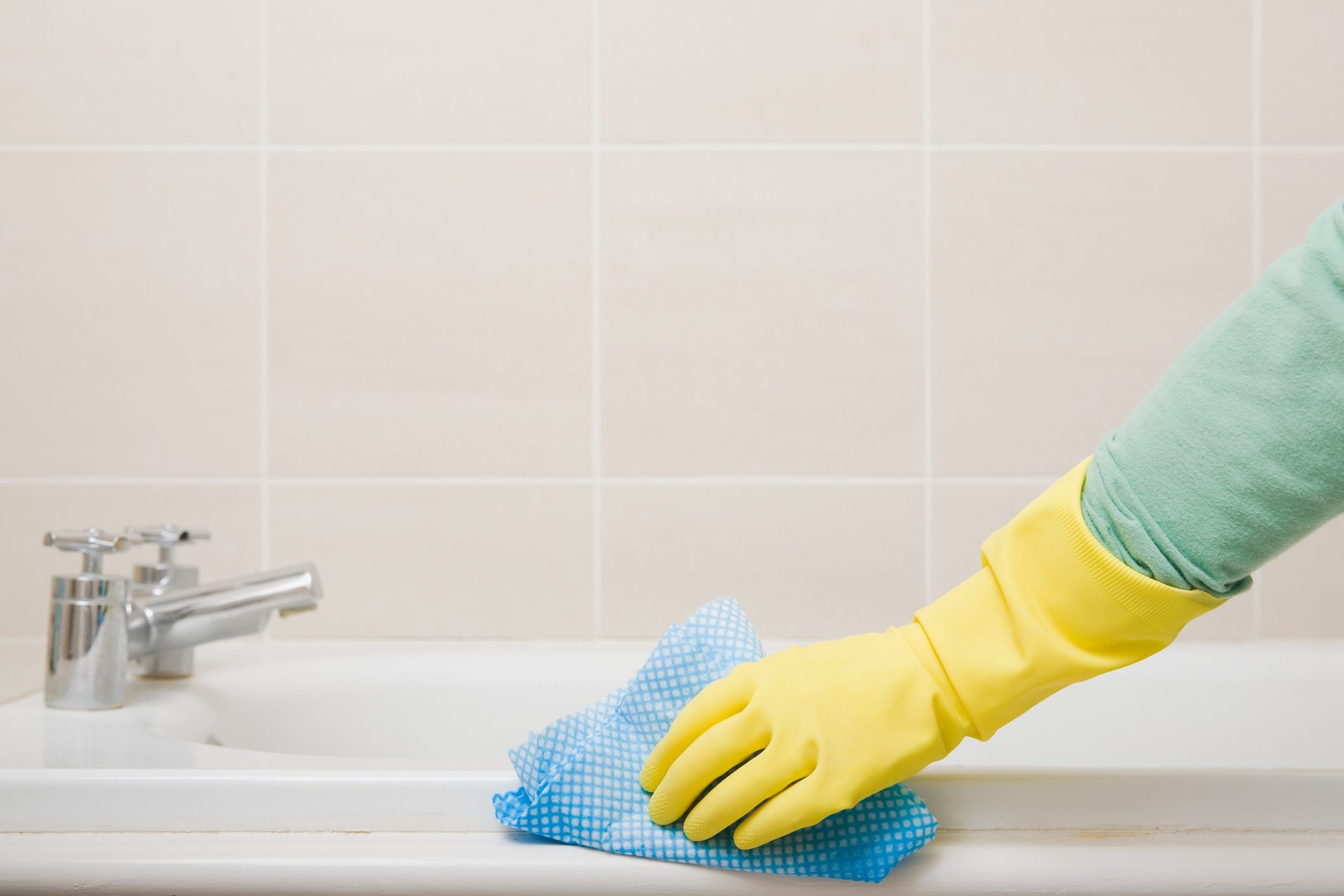 close up of rubber glove hand cleaning bathroom tile and grout