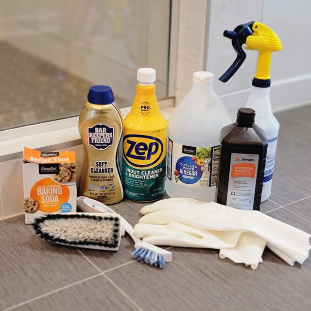various tile and grout cleaning products and tools on the floor of bathroom
