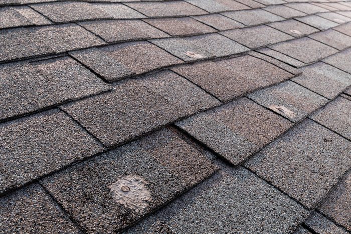 A wide view of a bad patches on a residential asphalt shingled roof exposing the nail heads