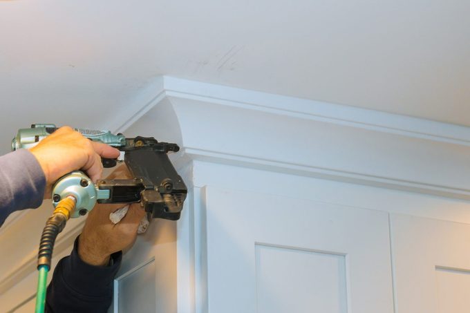 Air nailer tool carpenter using nail gun to crown moldings on kitchen cabinets with white cabinets