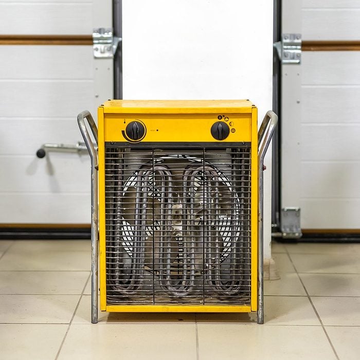 Big heavy industrial electric fan heater in double car garage interior. Two vehicles parked for winter storage in dry warm heating parking for cold winter season