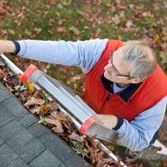 Man up ladder cleaning leaves out of gutter on house in autumn