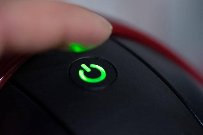 close up of person's finger touching green power button on appliance