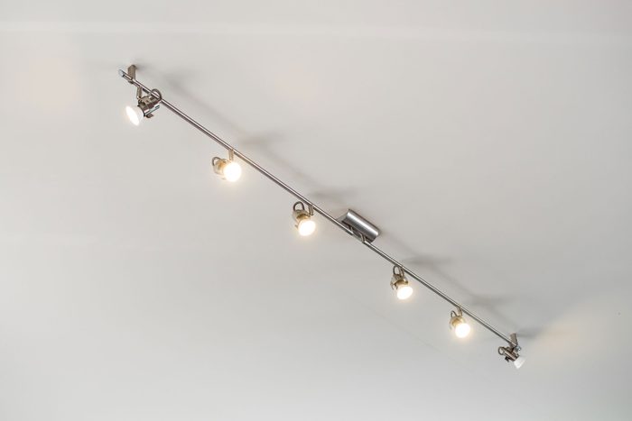 Modern stainless steel track light hanging on white ceiling background.