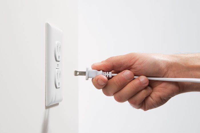 close up of hand holding plug near power outlet