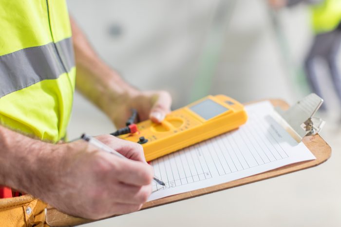Close-up of electrician taking notes on clipboard