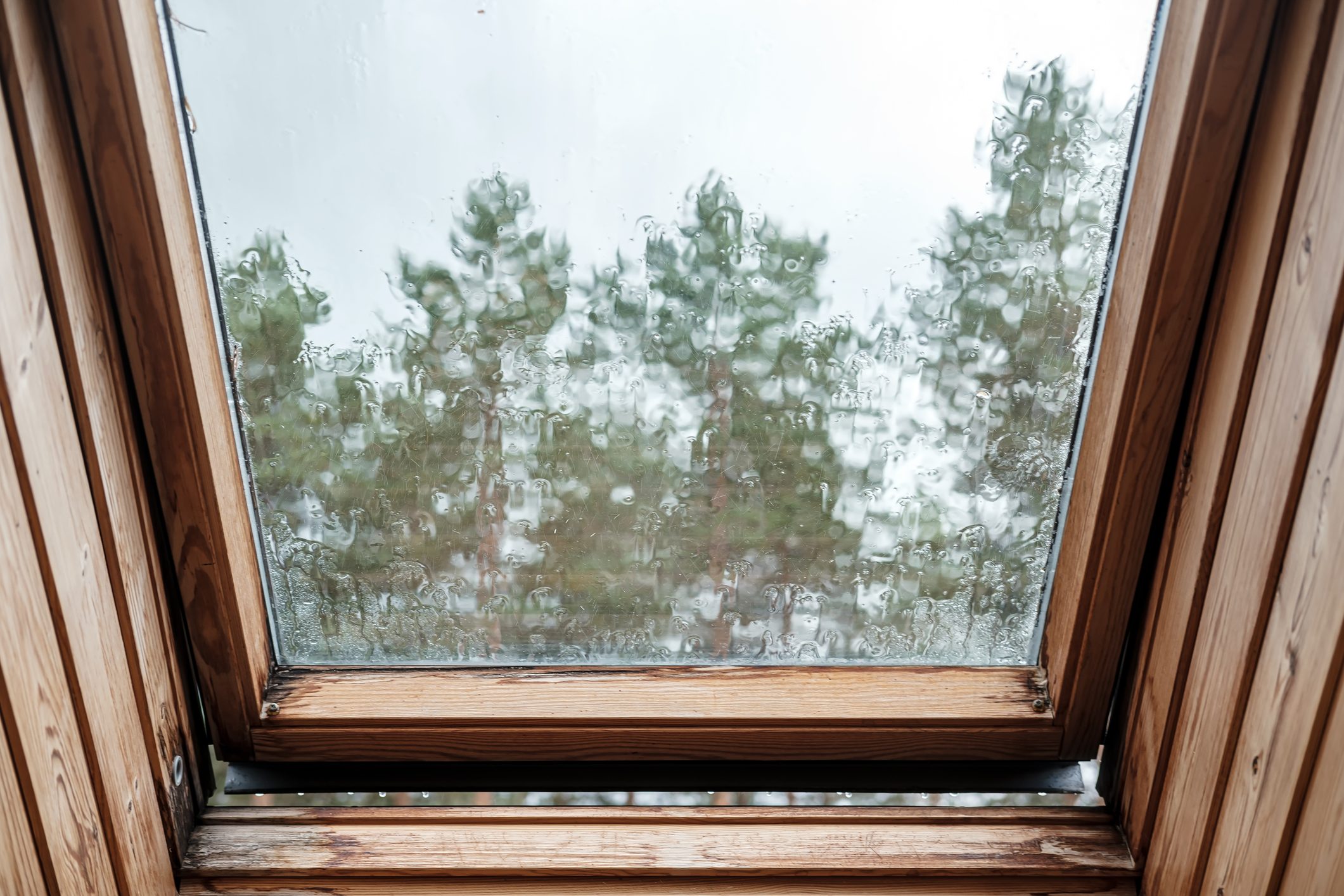 An ajar skylight window in the attic, with raindrops dripping down the glass and distorting the image.