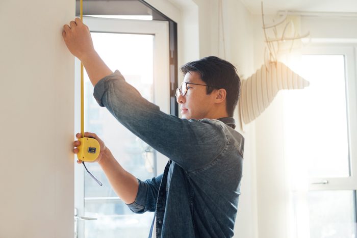 Young Man Doing DIY Using Measuring Tape At Home