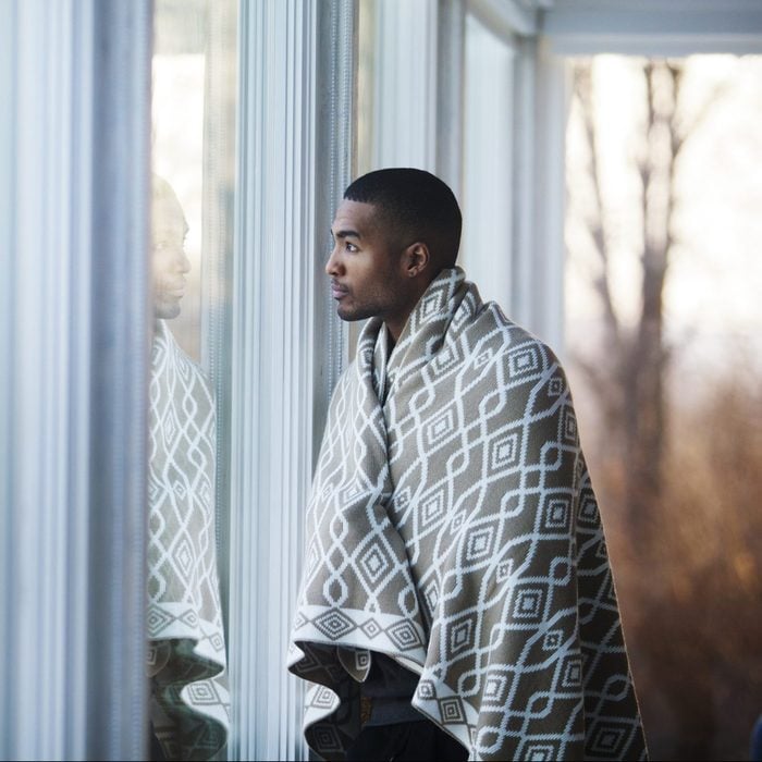 Man covered in blanket looking away while standing by window at home