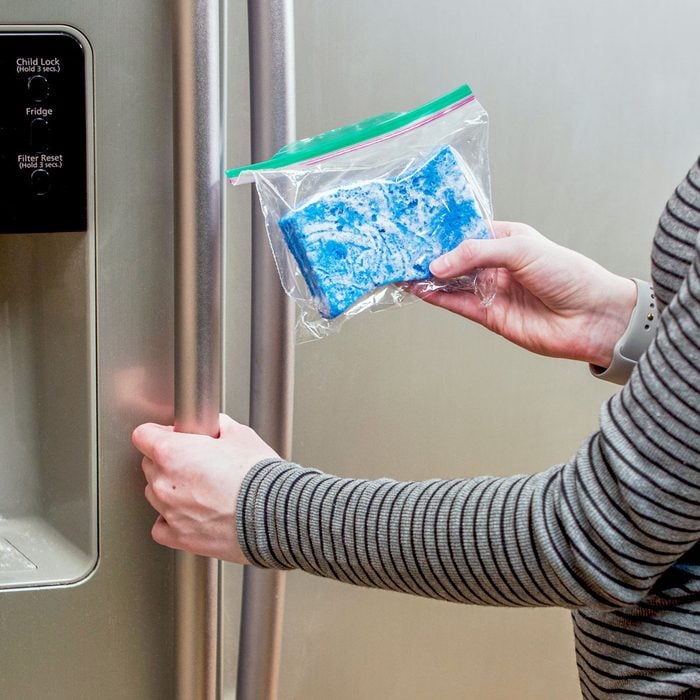 person holding a sponge inside a plastic ziplock bag standing near refrigerator doors