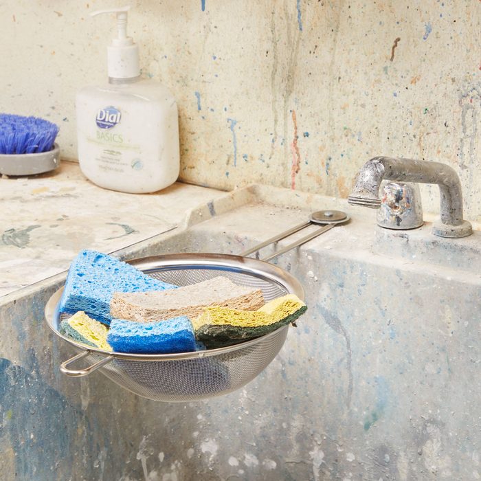 small metal sieve filled with sponges attached to a utility sink edge