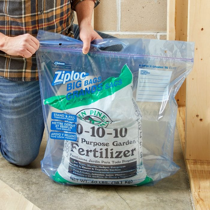 anonymous person sealing an extra large ziploc plastic bag with a bag of fertilizer inside in a garage setting