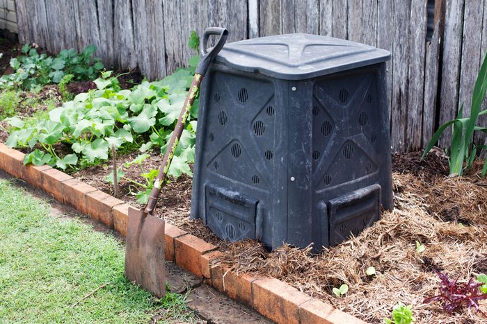 compost bin in a garden with a shovel leaning against it